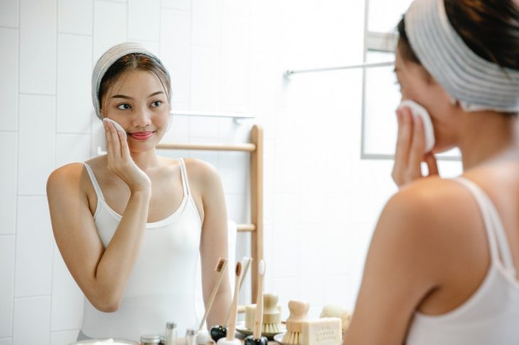 woman cleaning face with cotton pad