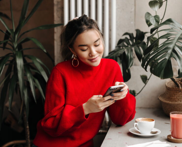 young woman chats on phone while sitting in cafe over cup of coffee