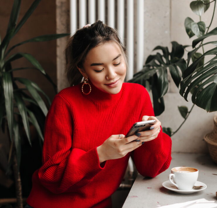 young woman chats on phone while sitting in cafe over cup of coffee