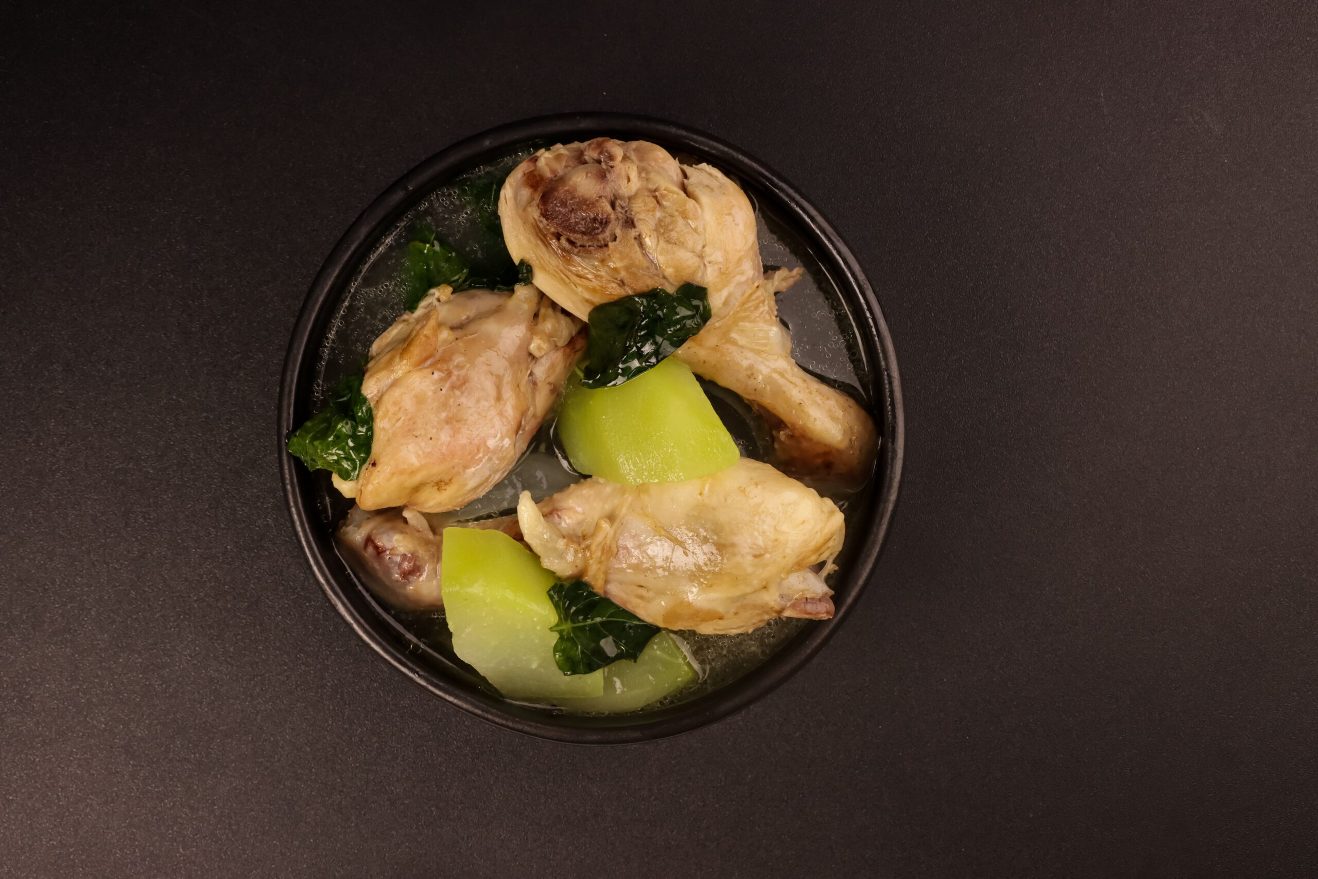 A comforting bowl of chicken tinola soup with ginger-infused broth, green papaya slices, and chili leaves.