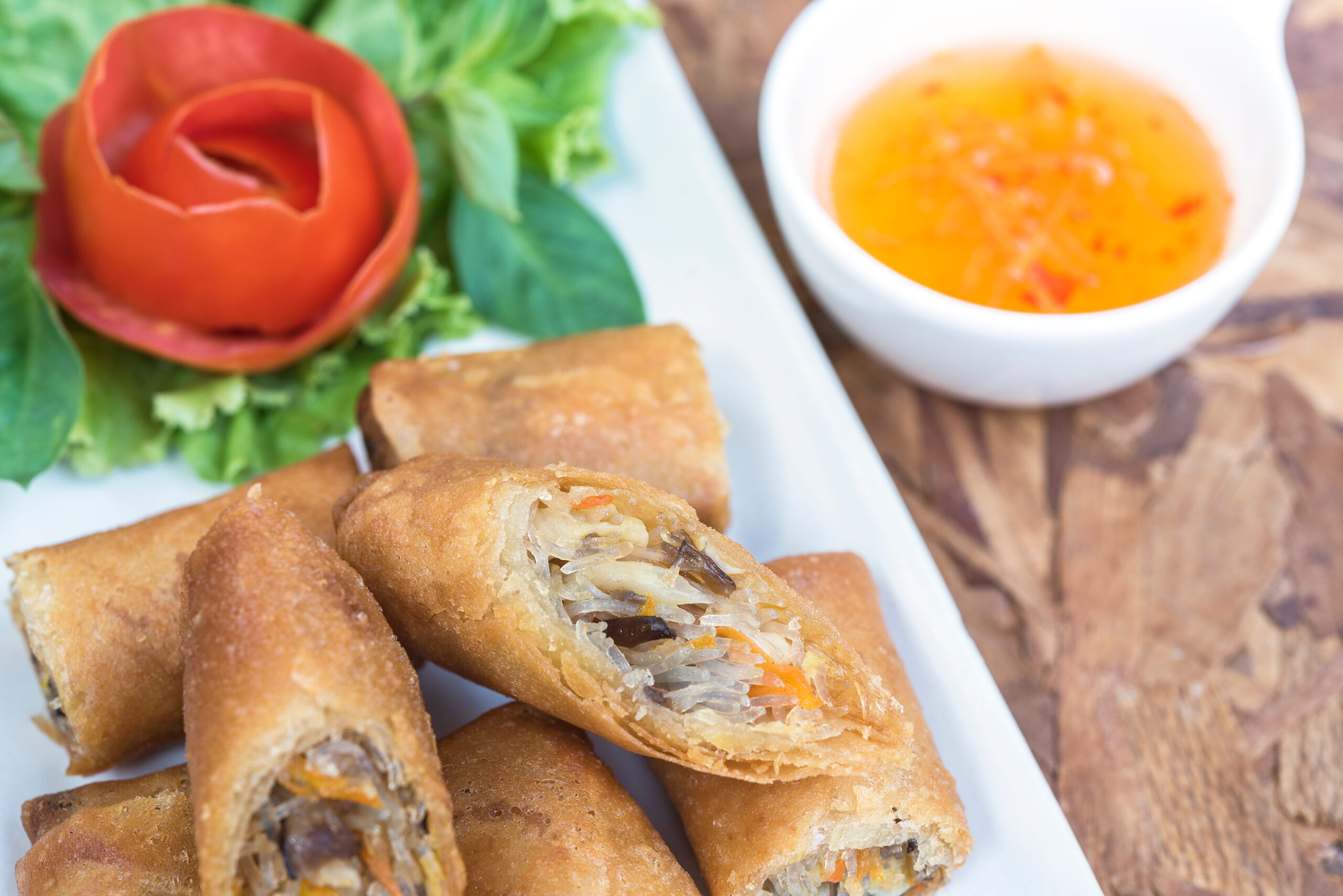 A platter of golden, crispy fried lumpia spring rolls cut in half, served with a sweet chili dipping sauce.