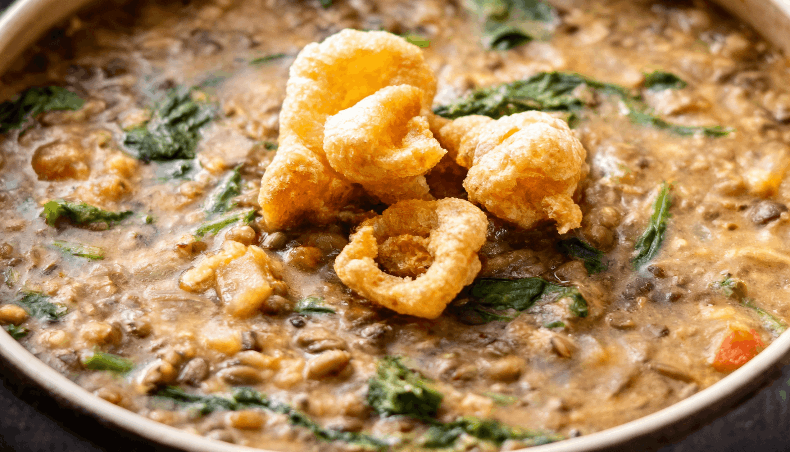 A hearty bowl of Filipino mung bean stew (ginisang monggo) cooked with spinach and topped with crispy chicharon.