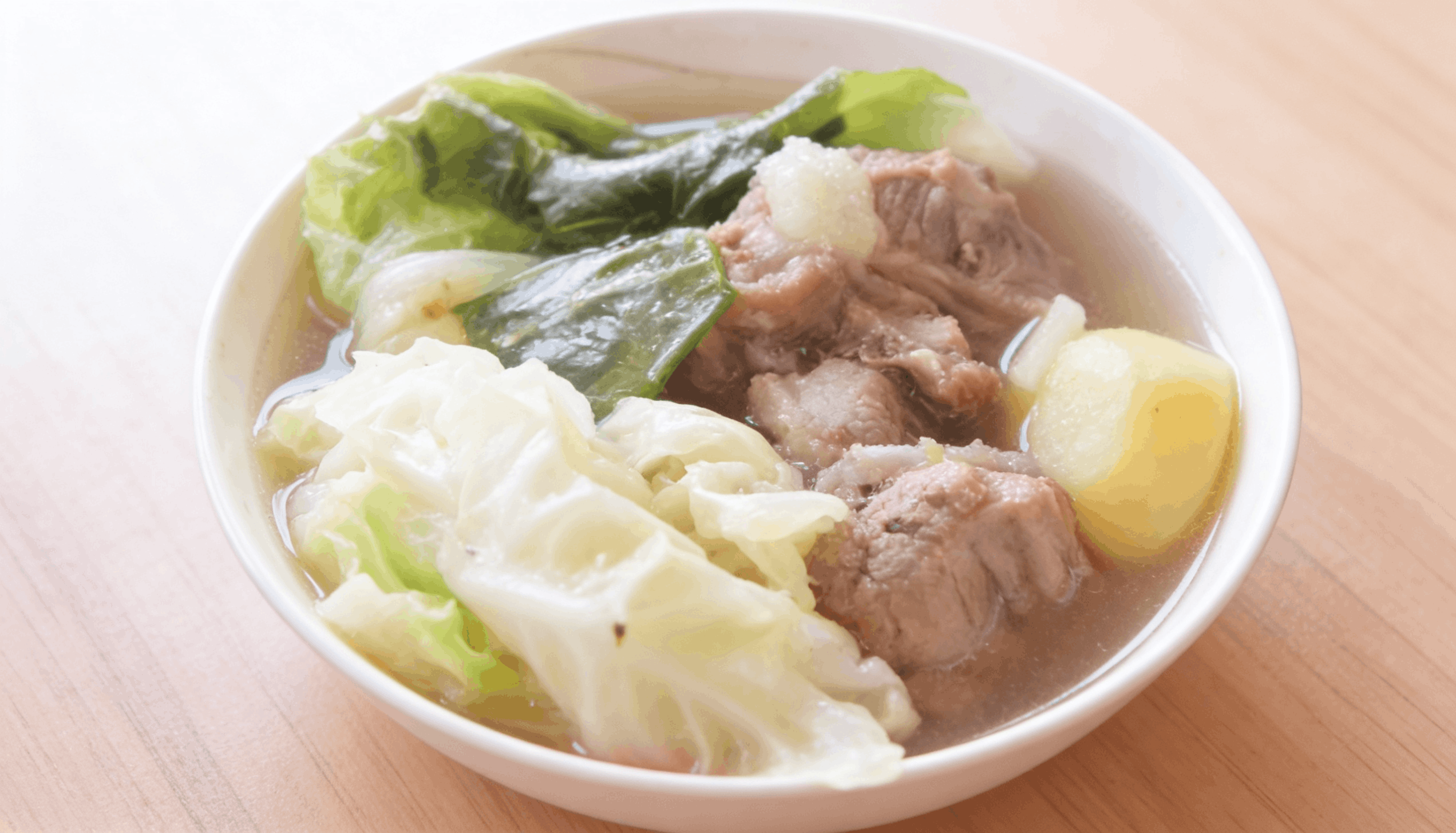 A clear broth pork soup (nilaga) with tender meat chunks, potatoes, green beans, and leafy cabbage.