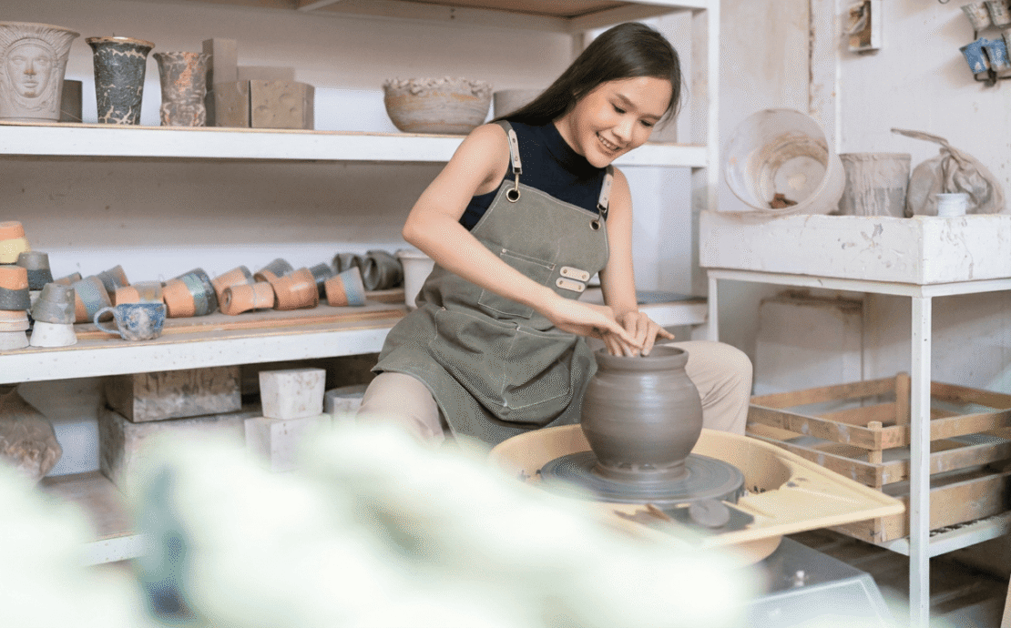 A woman shaping clay on a pottery wheel in a studio