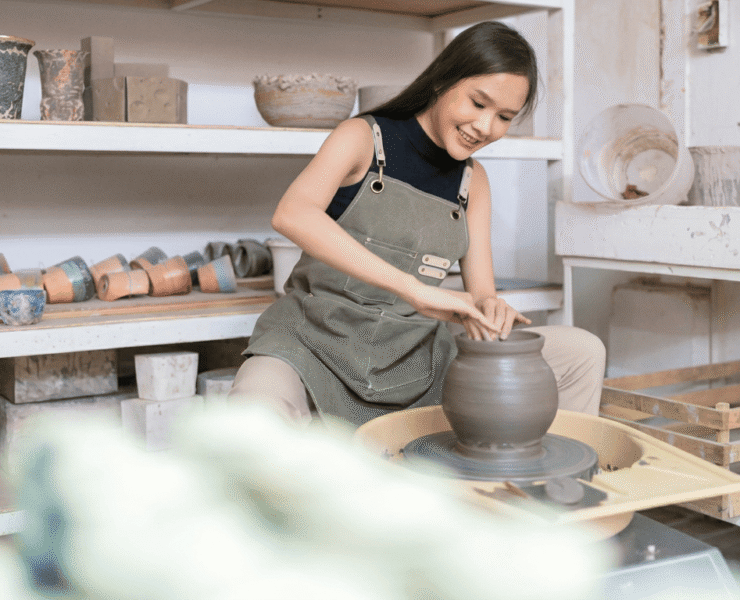 A woman shaping clay on a pottery wheel in a studio