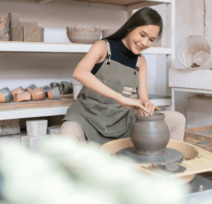 A woman shaping clay on a pottery wheel in a studio