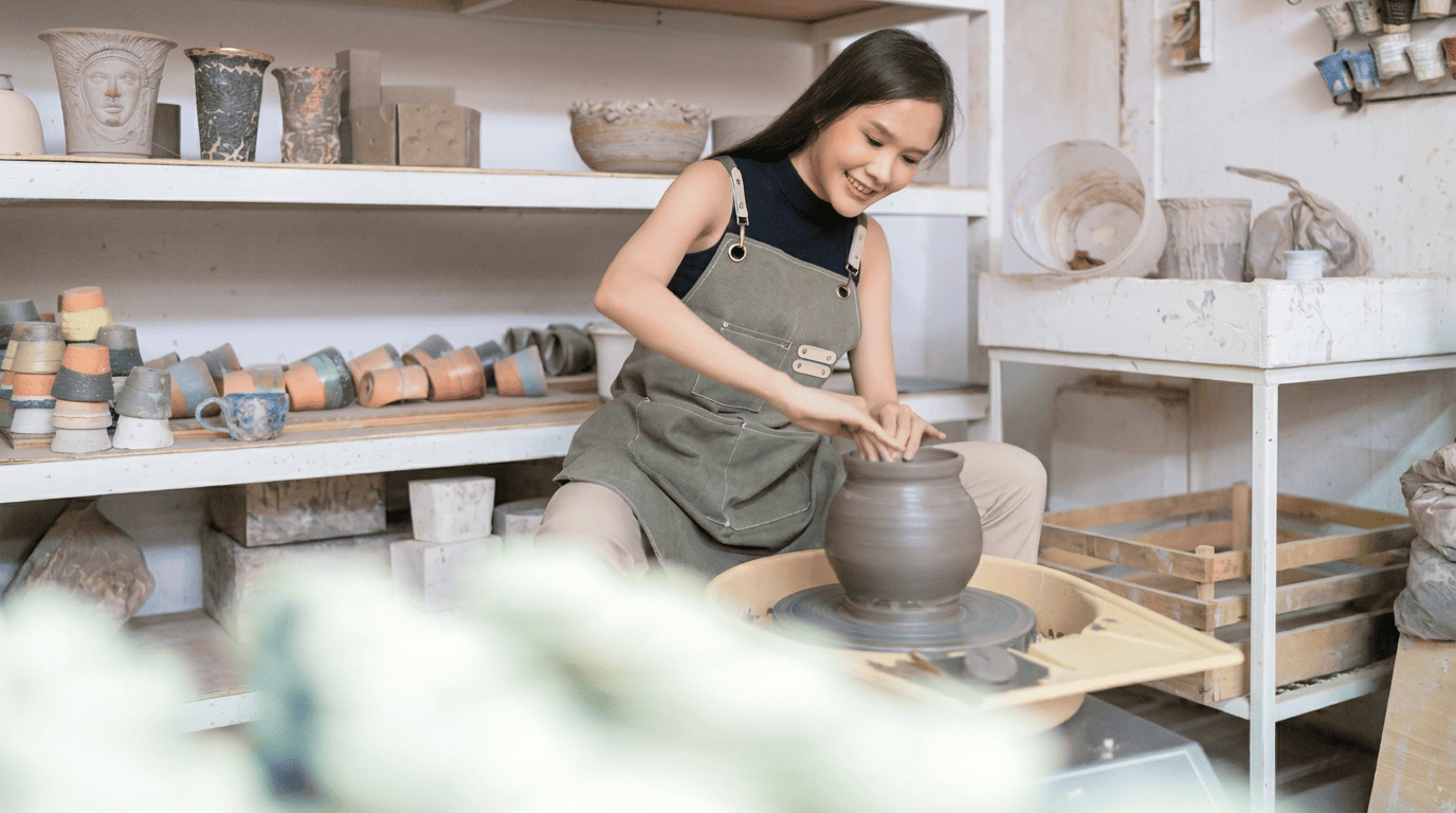 A woman shaping clay on a pottery wheel in a studio