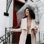 A woman in a camel coat holding a clear umbrella, a stylish rainy day outfit for work