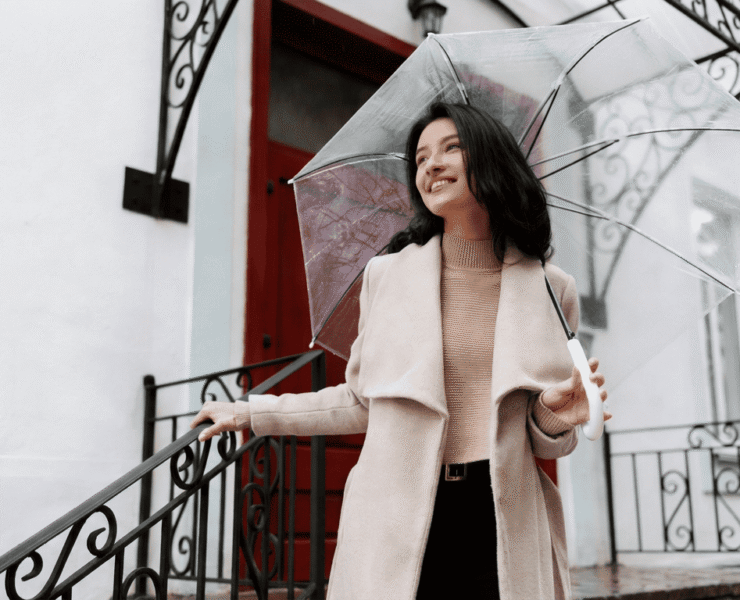 A woman in a camel coat holding a clear umbrella, a stylish rainy day outfit for work