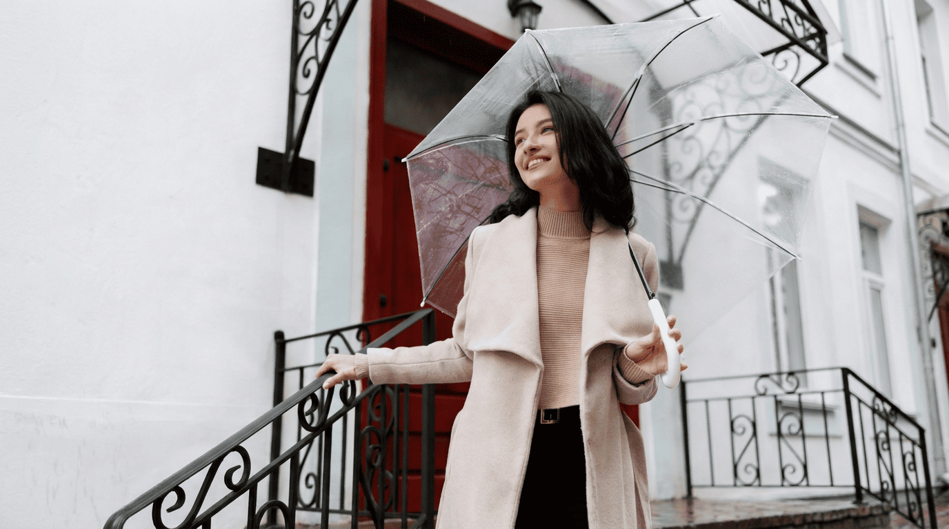 A woman in a camel coat holding a clear umbrella, a stylish rainy day outfit for work