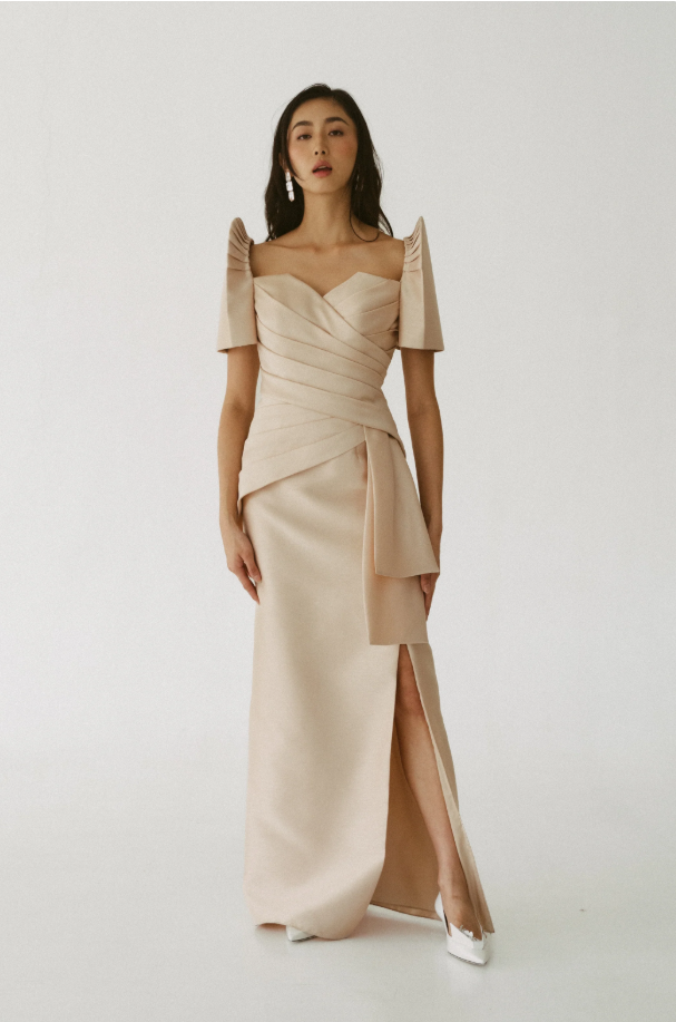 Woman in champagne satin gown with draped bodice, puff sleeves, and thigh-high slit, studio shot.