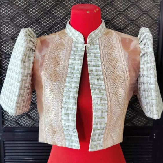 A cropped modern Filipiniana bolero jacket with green-and-beige woven patterns and butterfly sleeves displayed on a red mannequin