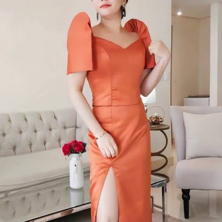 woman wearing an orange two-piece modern Filipiniana dress with structured butterfly sleeves and a side slit.