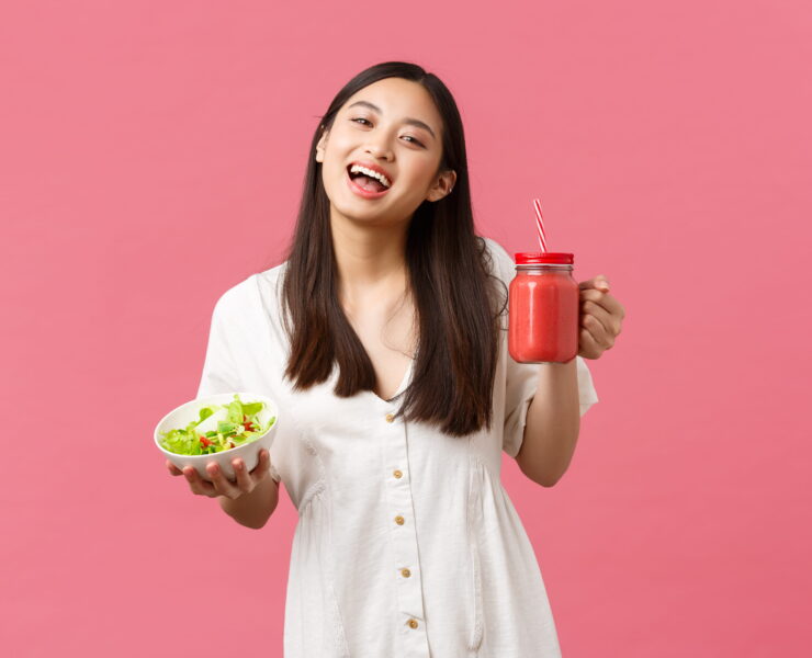 Smiling woman holding salad and smoothie
