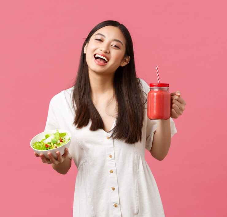 Smiling woman holding salad and smoothie