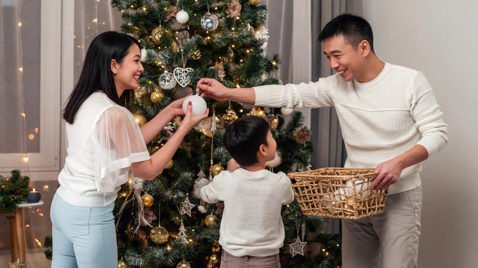 A family smiling together while hanging ornaments on a decorated Christmas tree.