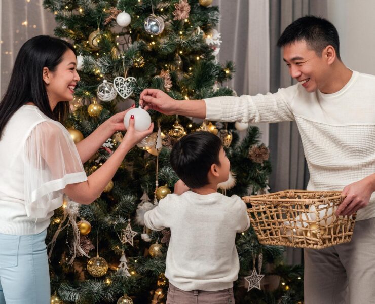 A family smiling together while hanging ornaments on a decorated Christmas tree.